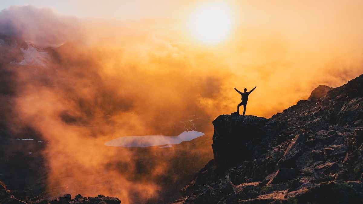 Man stands triumphant on a mountain in sunset.